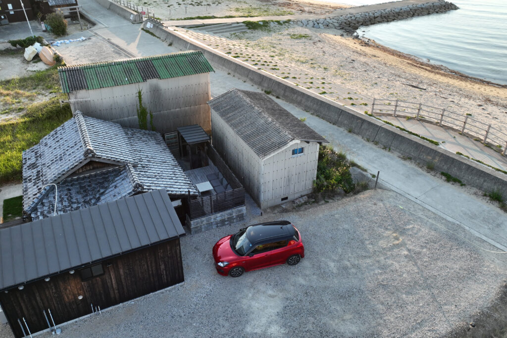 淡路島の海まで徒歩10秒の一棟貸し古民家宿 AKIYA nehemiah。瓦屋根の建物と駐車スペース、目の前の砂浜と海を写した空撮写真。